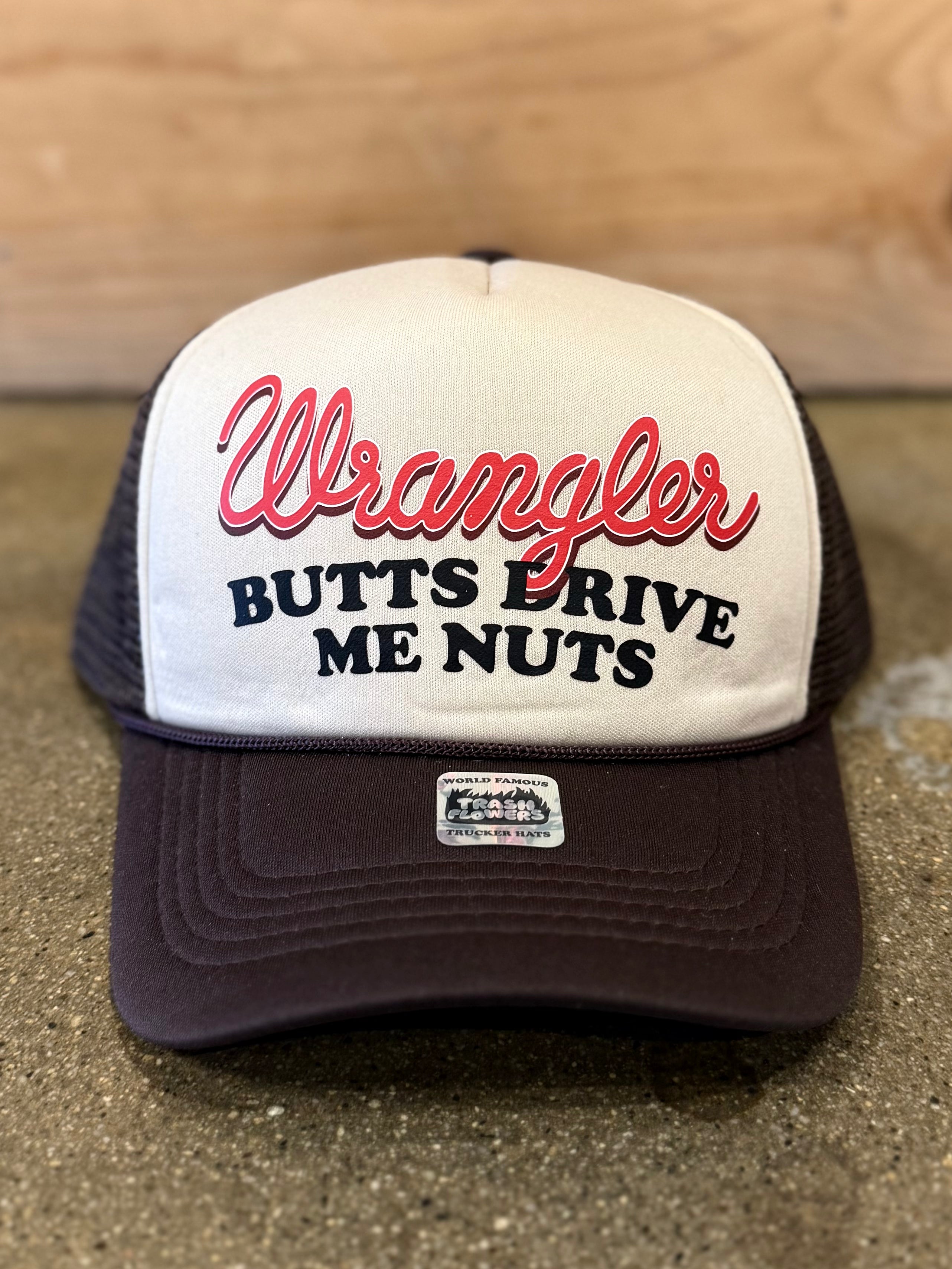 A beige and brown trucker hat with red and black lettering. The front panel says "Wrangler BUTTS DRIVE ME NUTS" in a bold and playful font. The cap features a mesh back